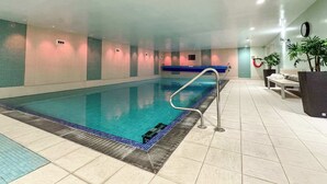 Ein Innenpool mit blau gefliestem Boden, einer Metallleiter und einer Sitzbank an der Wand.
