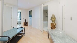 A hallway with a mirrored wardrobe, a bench with shoes, a guitar, and a Buddha statue. - Eclectically Curated 2BD Flat in Canary Wharf (Greater London)