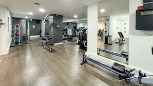 A gym with various exercise equipment, a large mirror, and a clock on the wall. - Eclectically Curated 2BD Flat in Canary Wharf (Greater London)