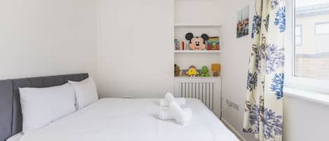 A bedroom with a bed, a radiator, a shelf with toys, and a window with curtains.