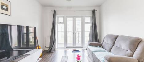 A living room with a sofa, a coffee table with a flower, a TV, and a window with curtains.