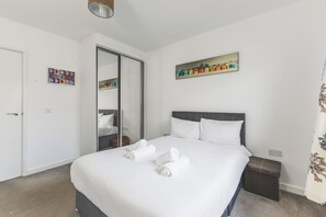 A hotel room with a bed, a wardrobe, a mirror, and a painting on the wall. - Modern two-bedroom flat, fully equipped (Greater London)