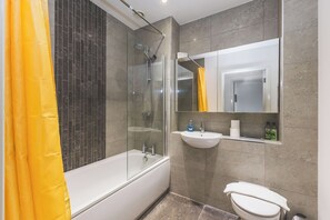 A bathroom with a bathtub, a glass-enclosed shower, a sink, and a toilet. - Modern two-bedroom flat, fully equipped (Greater London)