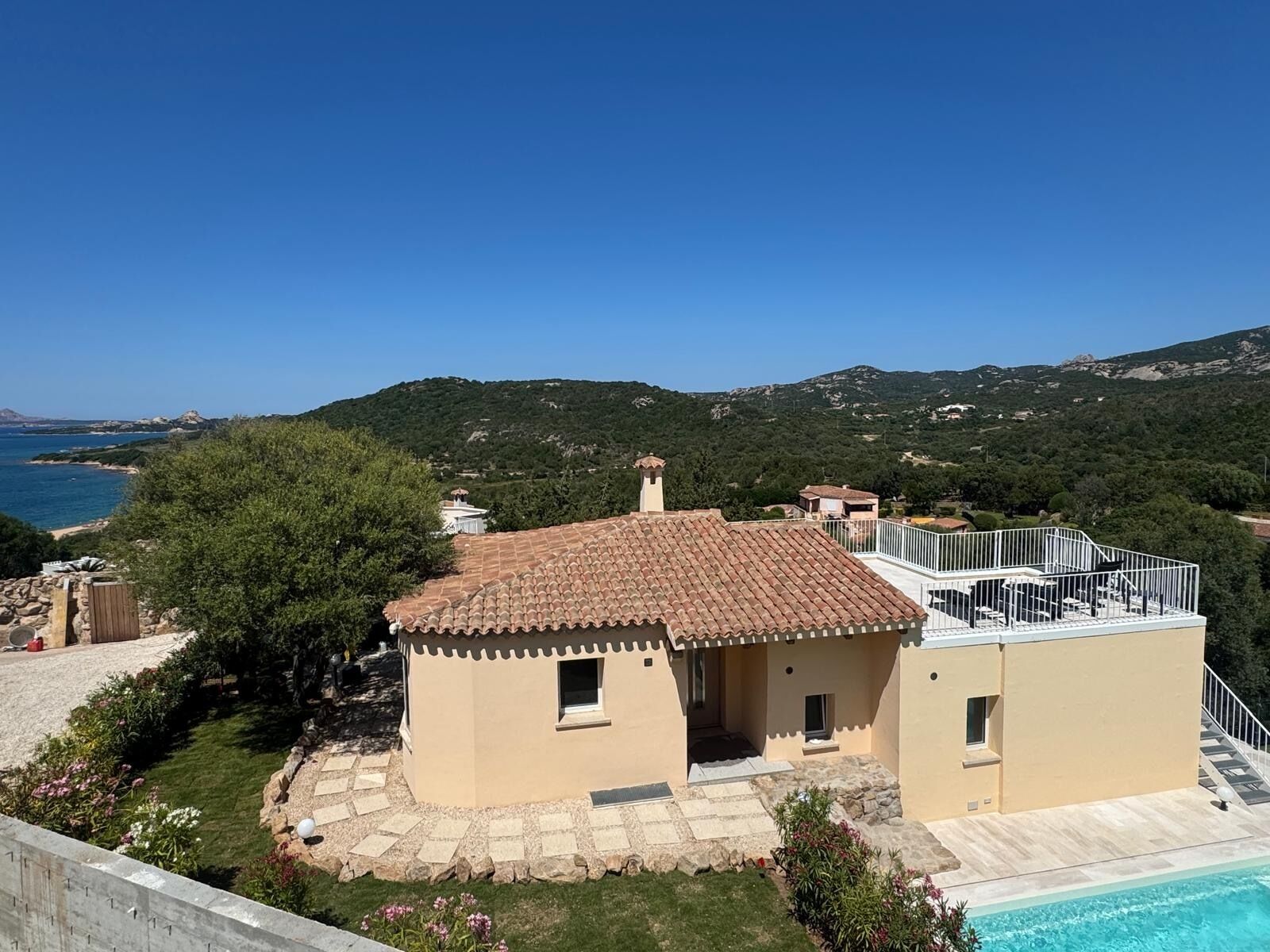 A Mediterranean-style villa with a swimming pool, terracotta roof, and a view of the sea and hills.