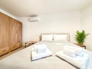 A modern hotel room with a large bed, a wooden wardrobe, a small bedside table, a potted plant, and an air conditioning unit. - Modern new Villa with 4 bedrooms and sea views. With private Pool (2026) (Sassari)