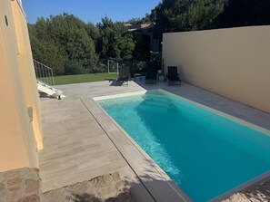 A rectangular swimming pool with a tiled deck, surrounded by a low wall and a grassy area with trees. - Modern new Villa with 4 bedrooms and sea views. With private Pool (2026) (Sassari)