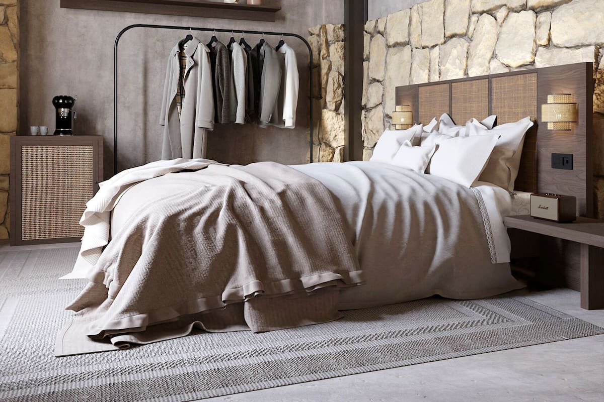 A bedroom with a stone wall, a bed with a white comforter, a wooden ceiling, and a hanging coat rack.