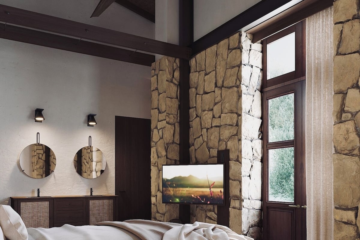 A bedroom with a stone wall, a large bed, a TV, and a ceiling fan.
