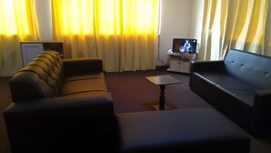 A living room with a sofa, a television, and curtains. - Accra City Guest House (Accra North)