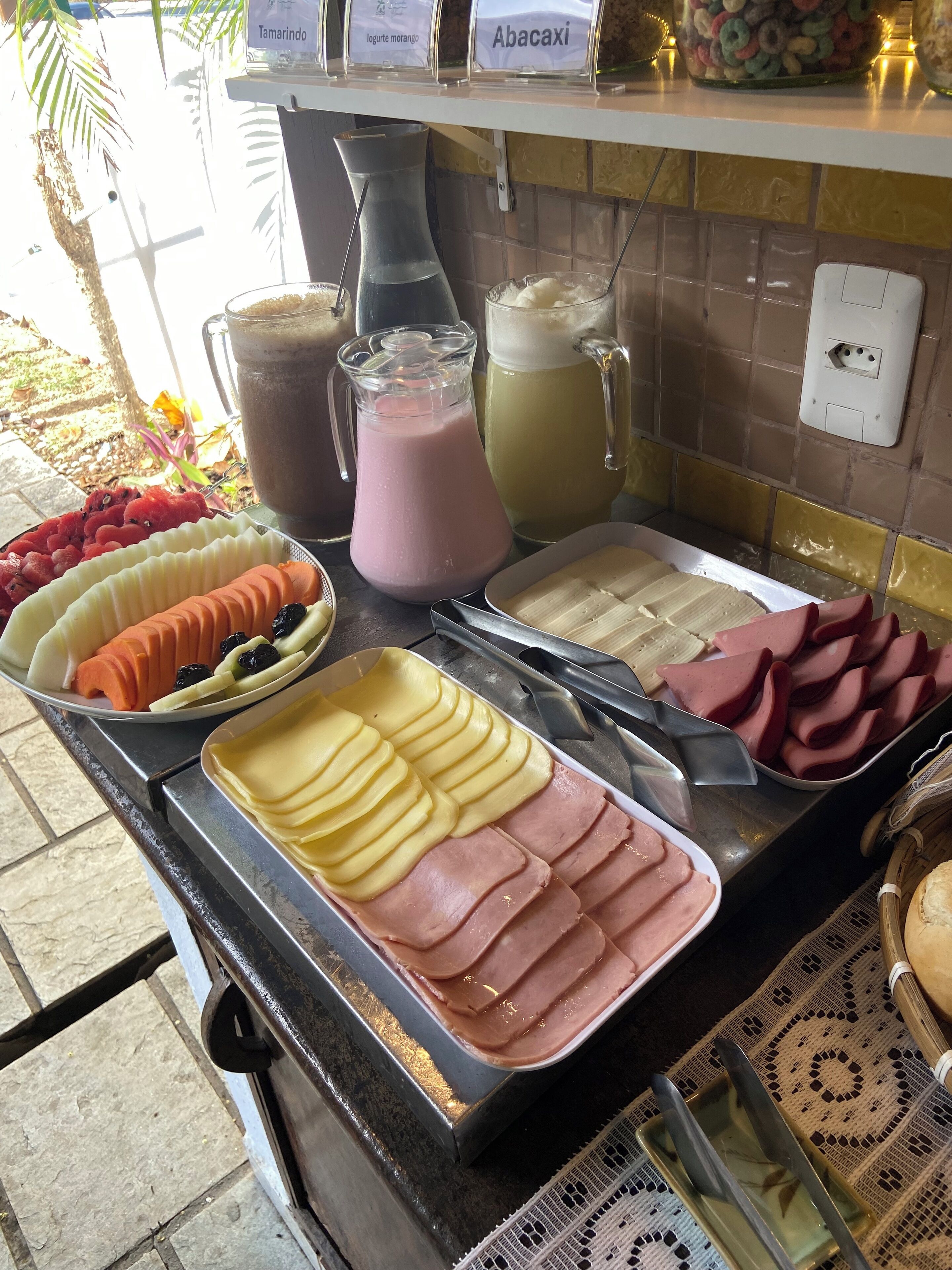 A buffet counter with various food items including sliced apples, ham, and a selection of juices.