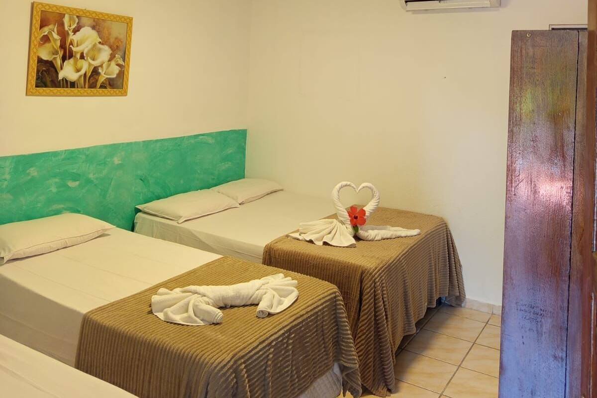 A hotel room with two beds, a teal headboard, a painting of flowers, an air conditioning unit, and a wooden door.