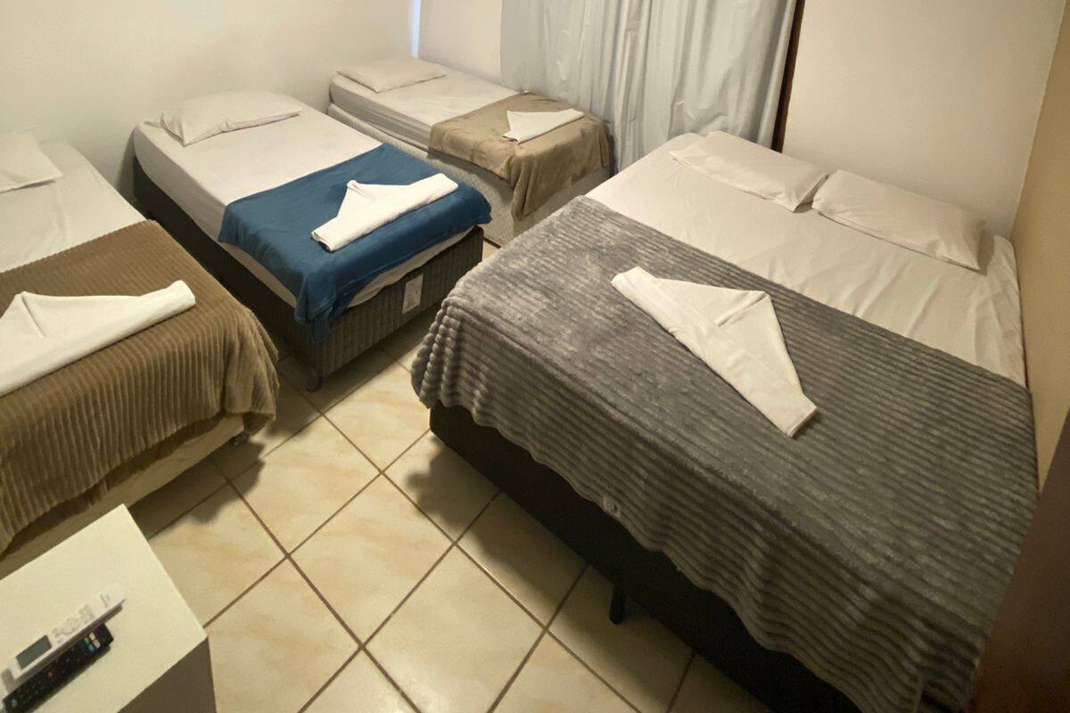 A hotel room with three beds, a small table with a remote control, and a painting on the wall.