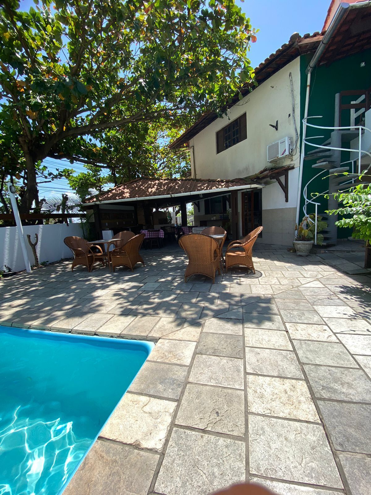 A covered outdoor patio with wicker furniture, a swimming pool, and a building with a tiled roof and windows.