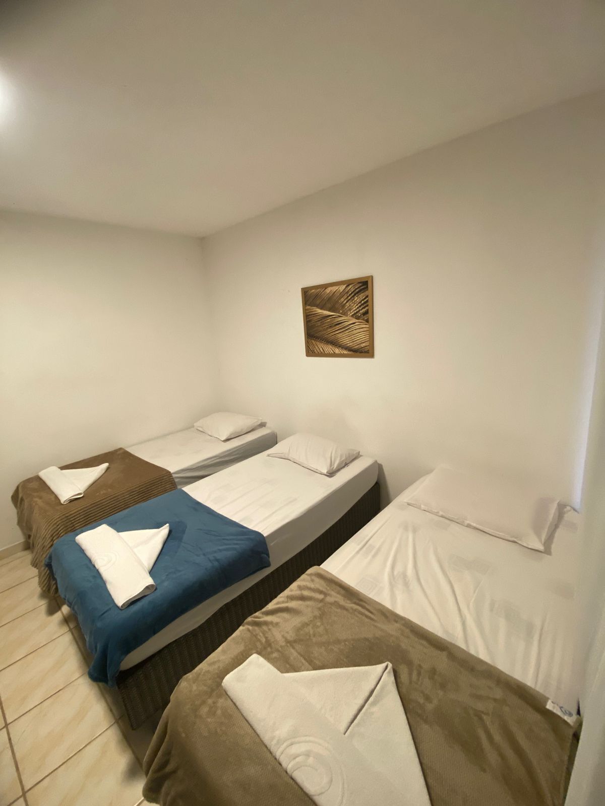 Ett hotellrum med tre sängar placerade i en rad, ett litet konstverk på väggen ovanför den mittersta sängen och ett klinkergolv.
