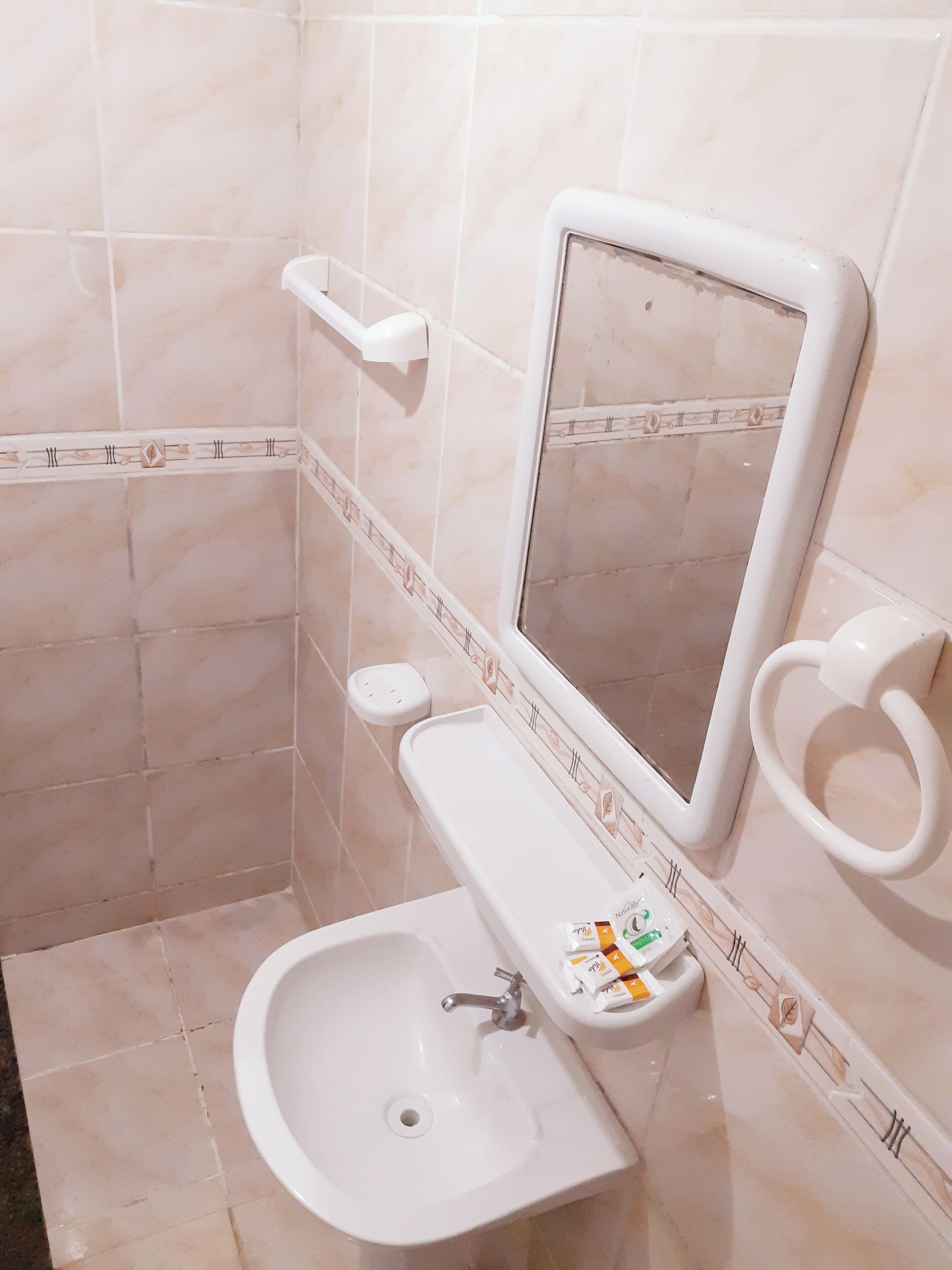 A bathroom with a sink, mirror, toilet, and hand soap dispenser.