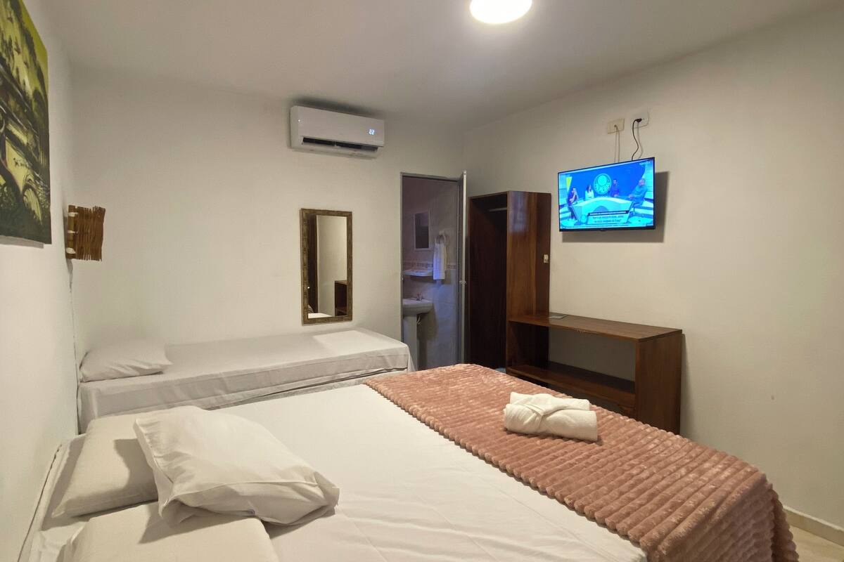 A hotel room with two beds, a TV, an air conditioner, and a mirror.
