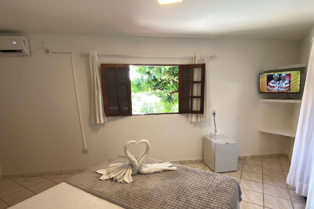 A hotel room with a bed, a window with curtains, a TV on a stand, and a small bedside table.