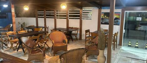 A restaurant with wooden tables and wicker chairs, a tiled floor, and a glass door leading outside.