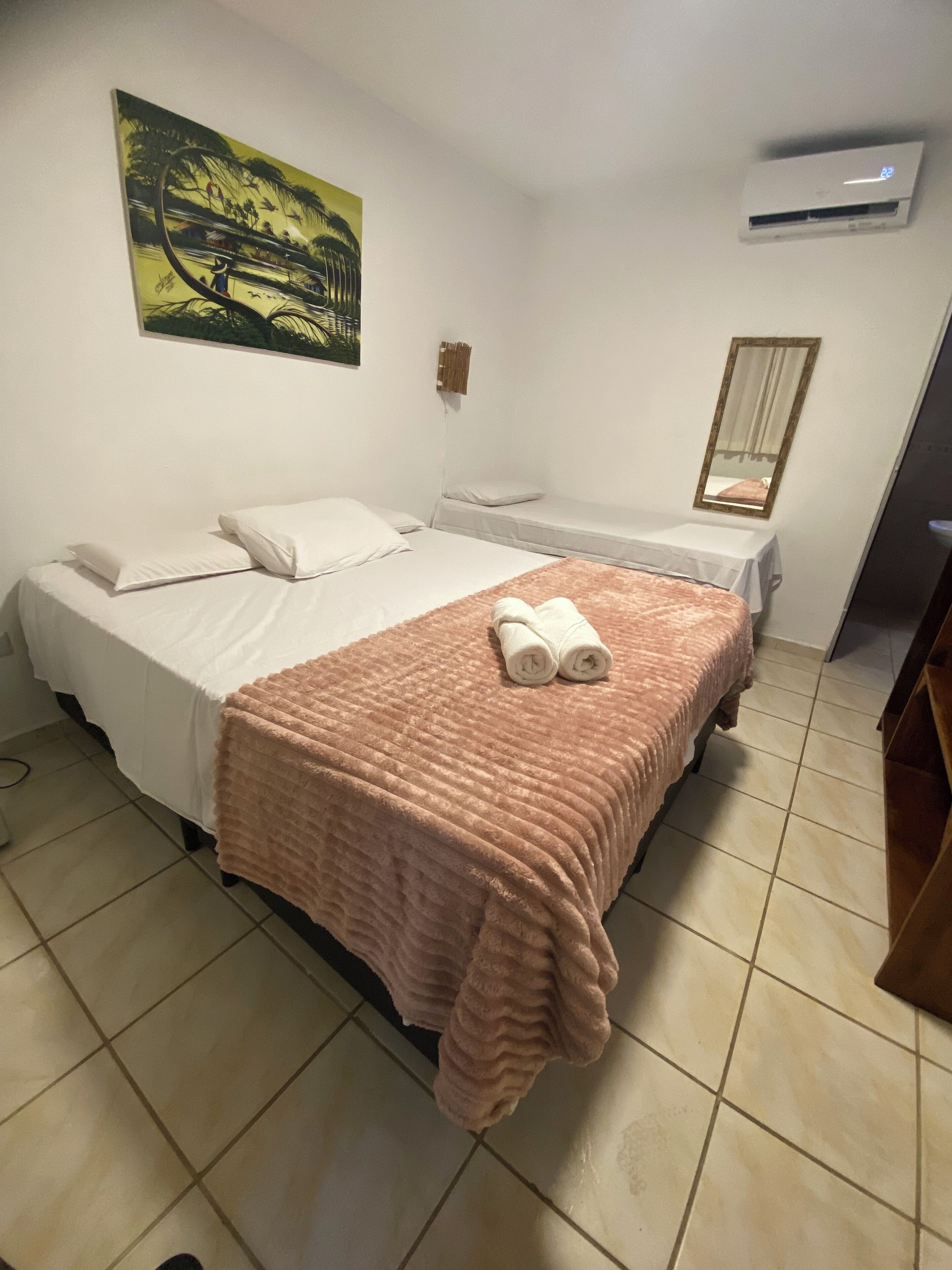 A hotel room with two beds, a large painting on the wall, an air conditioning unit, and a mirror.