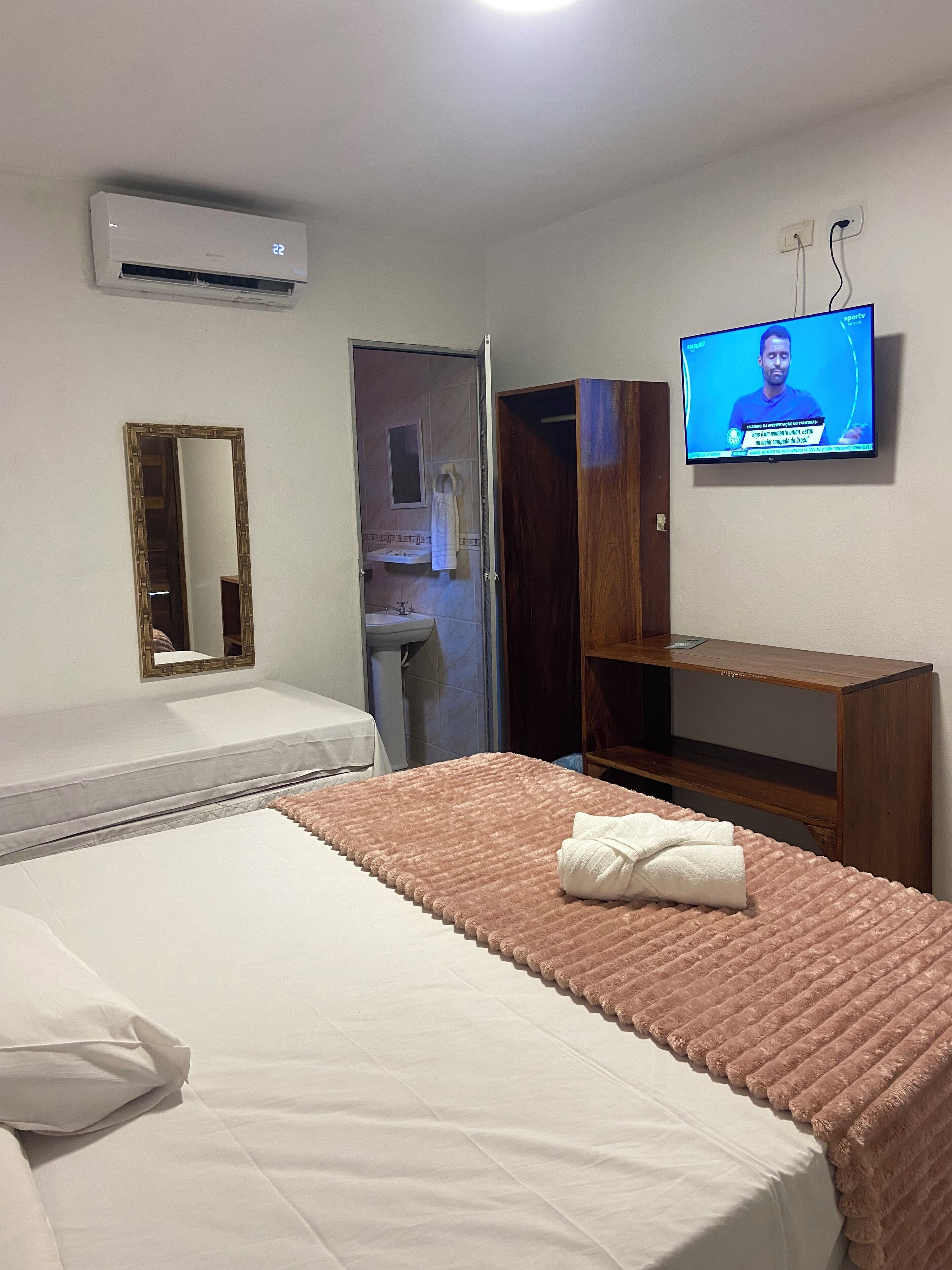 Una camera d'albergo con un letto, una televisione a muro, un armadio e un bagno visibile attraverso una porta aperta.