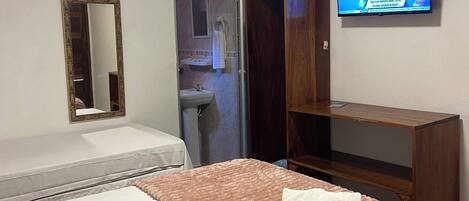 Una camera d'albergo con un letto, una televisione a muro, un armadio e un bagno visibile attraverso una porta aperta.