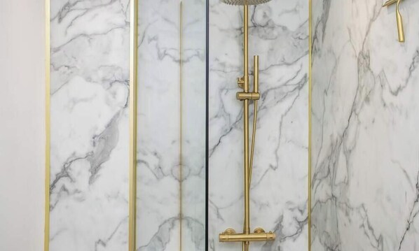 Une salle de bain avec un mur en marbre et une robinetterie de douche dorée.