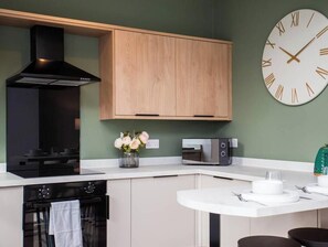 A kitchen with a built-in oven, a microwave, and a clock on the wall. - Vacant Nests | The Jackson | Wi-Fi | Parking (Tynemouth)