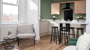A modern kitchen with wooden cabinets, a black range hood, and a bar area with stools. - Vacant Nests | The Jackson | Wi-Fi | Parking (Tynemouth)