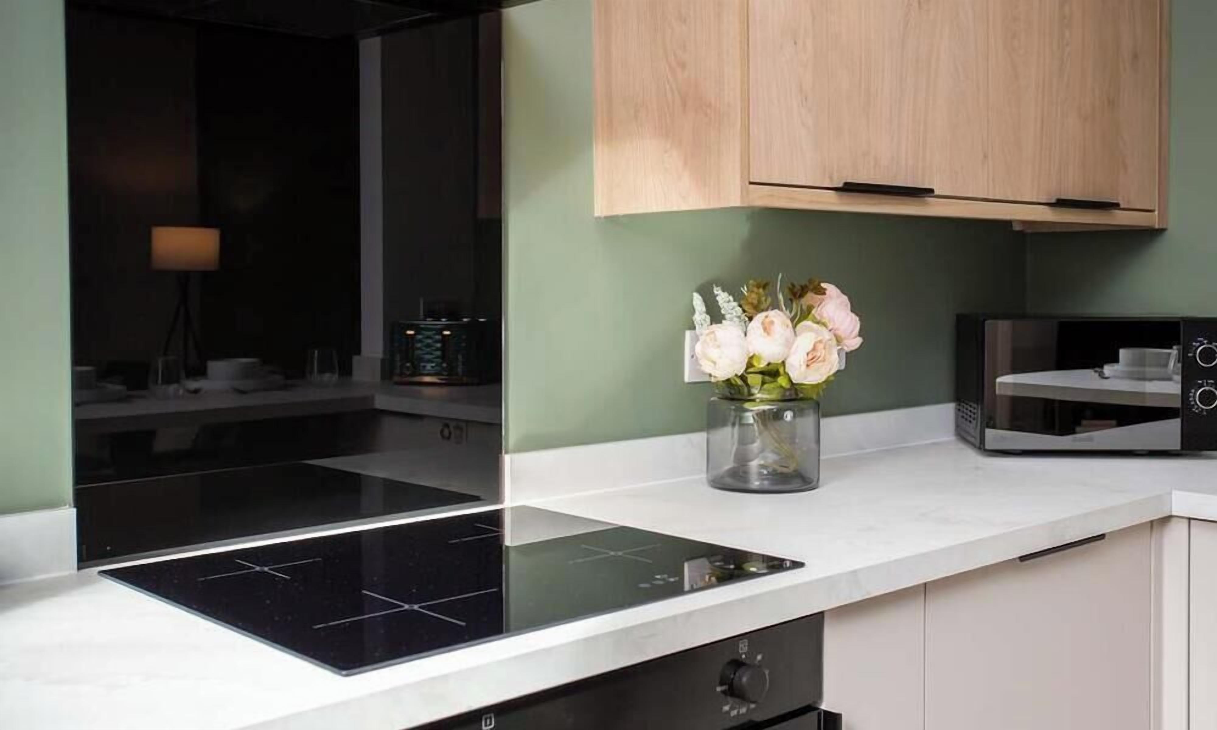 Cozinha moderna com fogão por indução preto, armários de madeira e um vaso de flores na bancada.