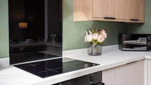 A modern kitchen with a black induction cooktop, wooden cabinets, and a vase of flowers on the countertop. - Vacant Nests | The Jackson | Wi-Fi | Parking (Tynemouth)