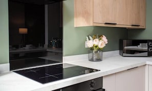 A modern kitchen with a black induction cooktop, wooden cabinets, and a vase of flowers on the countertop.