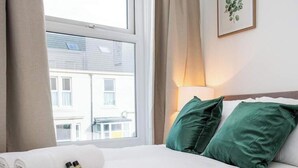 A hotel room with a bed, a window, a lamp, and a framed picture on the wall. - Vacant Nests | The Jackson | Wi-Fi | Parking (Tynemouth)