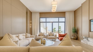A modern living room with a beige sofa set, a coffee table, and a large window with a view of buildings and trees.