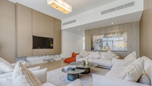 A modern living room with a large flat-screen TV, a marble fireplace, and a large window with a view of the city.