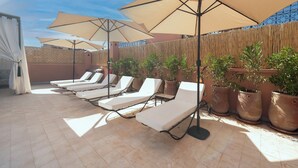 Eine Dachterrasse mit Liegestühlen und großen Sonnenschirmen, umgeben von Topfpflanzen und einem Bambuszaun.