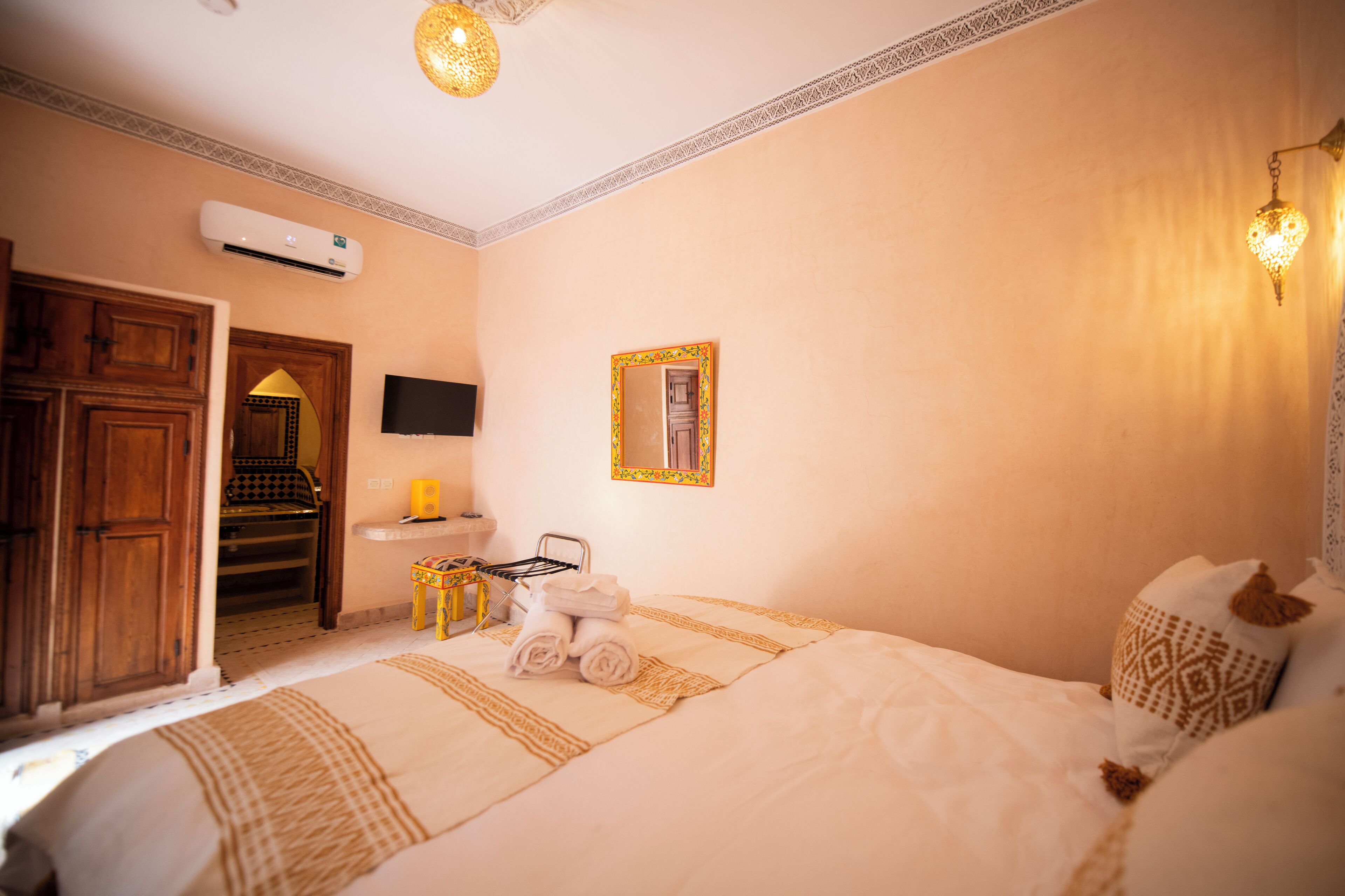A hotel room with a bed, a TV, a mirror, a small table with towels, and a door leading to a bathroom.