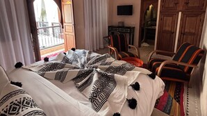 Ein Schlafzimmer mit einem Bett, zwei Stühlen, einem Fernseher und einer dekorativen Deckenleuchte.