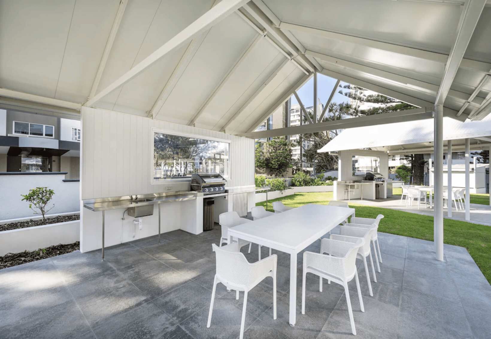 Un espace cuisine extérieur avec une longue table et des chaises, un barbecue et un évier.