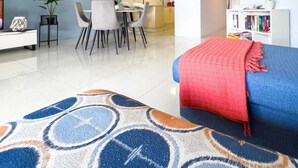 A modern living room with a blue sofa, a patterned rug, a dining area with a table and chairs, and a kitchen in the background. - Beachfront Apartment with Hot Tub & Pool (Bilinga)