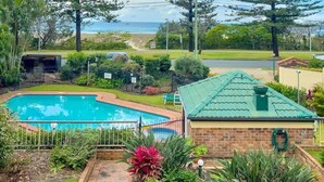 A swimming pool surrounded by lush greenery and tall trees, with a view of the ocean in the background. - Beachfront Apartment with Hot Tub & Pool (Bilinga)