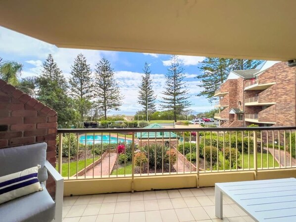 Un balcon avec vue sur une piscine, un jardin et les bâtiments voisins.