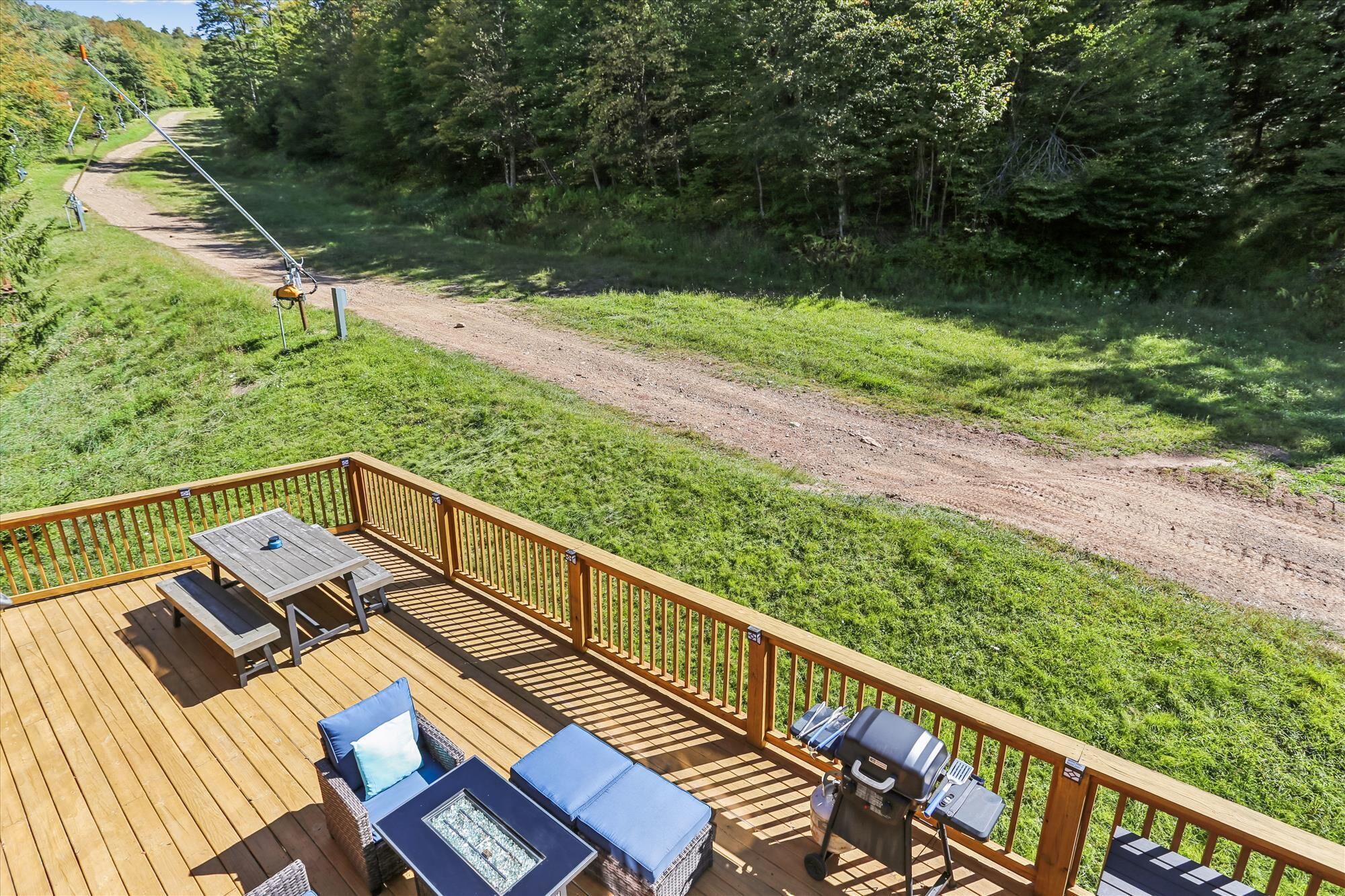 A deck with outdoor furniture, a grill, and a dirt path leading into a wooded area.