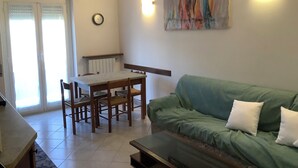 Een woonkamer met een groene bank, een eettafel met stoelen, een klok aan de muur en een schilderij boven de bank.