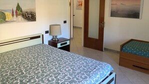 Een hotelkamer met een bed, een nachtkastje met een lamp, een klein nachtkastje, een stoel, een deur en een schilderij aan de muur.