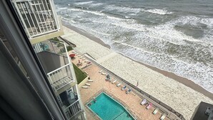 A view from a balcony overlooking a beach with a swimming pool and lounge chairs. - Welcome to your perfect beachfront condo in Daytona Beach Shores! (Daytona Beach Shores)
