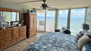 A bedroom with a large bed, a ceiling fan, a dresser, and a view of the ocean through large windows. - Welcome to your perfect beachfront condo in Daytona Beach Shores! (Daytona Beach Shores)