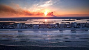 A coastal cityscape with high-rise buildings, a beach, and a sunset over the water. - Welcome to your perfect beachfront condo in Daytona Beach Shores! (Daytona Beach Shores)