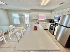 A modern kitchen with white cabinets, a stainless steel refrigerator, and a dining area with white chairs and a table.