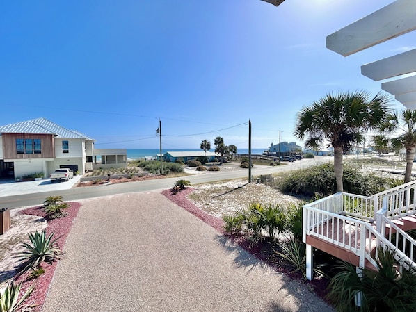 A coastal property with a driveway leading to a house, a beach view, and a staircase to a deck.