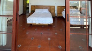Een slaapkamer met een groot bed, een houten hoofdeinde en een stenen muur. Er zijn twee hanglampen en een plafondventilator.